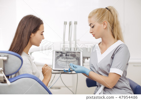 Dentist and patient choosing treatment in a consultation with medical equipment in the background Dentist and patient choosing treatment in a consultation with medical equipment in the background 47954486