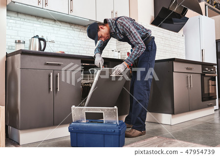 Service in time. Male technician sitting near dishwasher 47954739