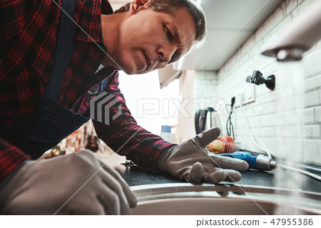 Inside view. Close-up of handsome plumber repairing sink in kitchen 47955386