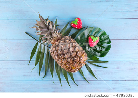 Tropical pineapple with homemade glazed cookies served on palm leaves on blue wooden background 47956383