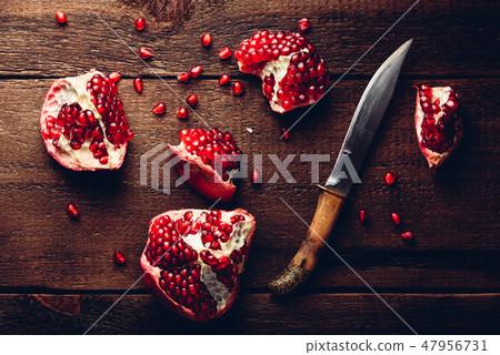 Pomegranate pieces with knife on wooden table 47956731
