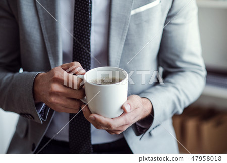 A midsection of businessman standing in an office, holding a cup of coffee. 47958018