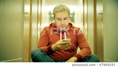 Grey haired young man in casual clothes using his smartphone in the hotel hallway 47969293