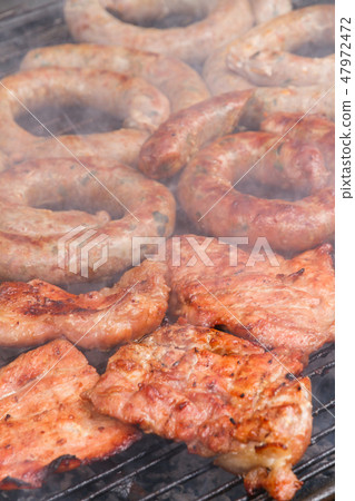 Grilled sausage and pork cooking on flaming grill. Grilled sausage and pork cooking on flaming grill. 47972472