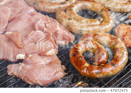 Grilled sausage and pork cooking on flaming grill. Grilled sausage and pork cooking on flaming grill. 47972475