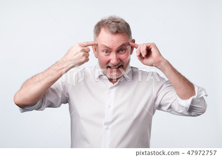 Angry senior man gesturing with his finger against temple asking are you crazy Angry senior man gesturing with his finger against temple asking are you crazy 47972757