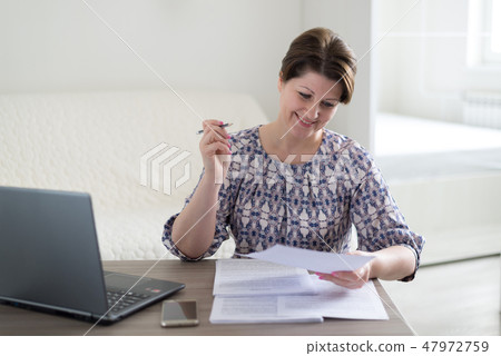 Woman working with documents looking at laptop Woman working with documents looking at laptop 47972759
