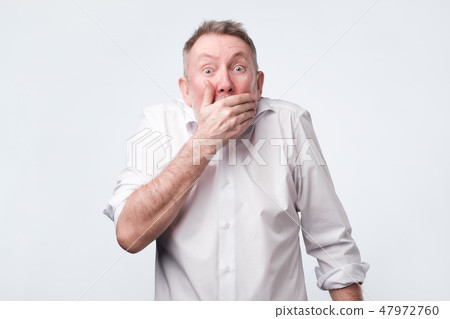 man in white shirt covering mouth with hand and looking at camera man in white shirt covering mouth with hand and looking at camera 47972760