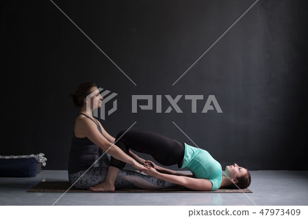 Young woman in ardha chakrasana yoga Pose. Teacher help her to do it. Young woman in ardha chakrasana yoga Pose. Teacher help her to do it. 47973409