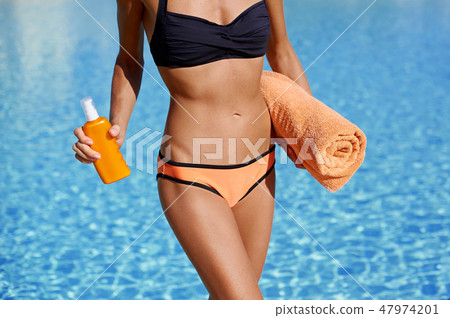 Attractive woman on the beach holding a towel and sunblock lotion sunscreen in her hands, summer sun 47974201