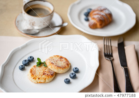 Cheesecake, fresh blueberry and cappuccino. Cottage cheese pancakes or curd fritters on white plate Cheesecake, fresh blueberry and cappuccino. Cottage cheese pancakes or curd fritters on white plate 47977188