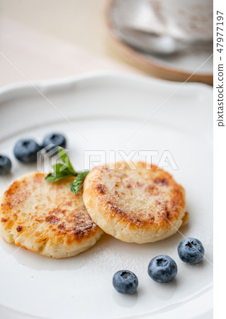 Cheesecake, fresh blueberry and cappuccino. Cottage cheese pancakes or curd fritters on white plate Cheesecake, fresh blueberry and cappuccino. Cottage cheese pancakes or curd fritters on white plate 47977197