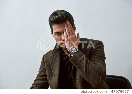 I'll just look. Stylish dark-haired man looking at camera while sitting on the chair over white 47979657