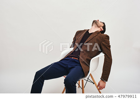 Sick and tired. Stylish dark-haired businessman sitting on a chair, leaning back and looking at the 47979911