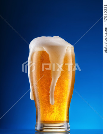 Glass of light beer with drip foam on blue background Glass of light beer with drip foam on blue background 47980331