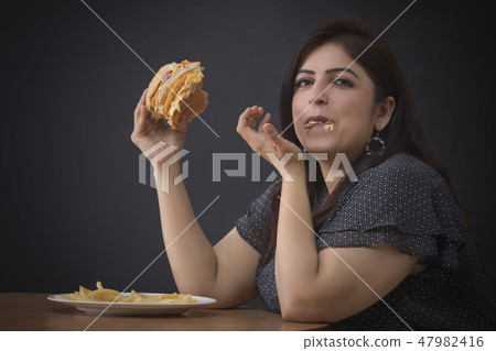 Fat woman eating a hamburger 47982416