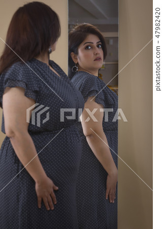 Obese Woman trying dress in looking in mirror Obese Woman trying dress in looking in mirror 47982420
