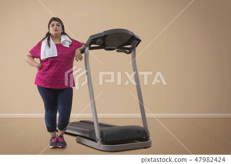 Overweight woman standing with treadmill 47982424