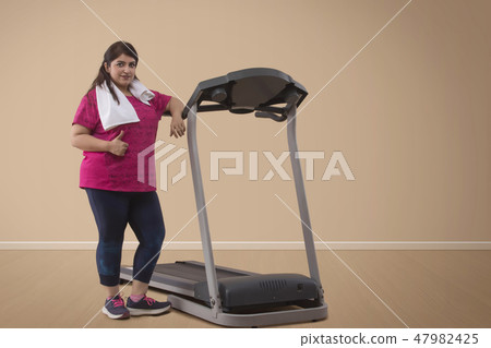 Overweight woman standing with treadmill 47982425