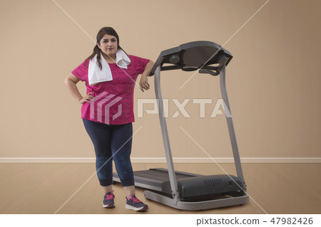 Overweight woman standing with treadmill 47982426