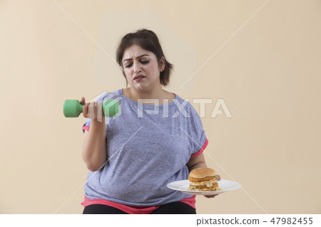 Sad Overweight Woman holding a burger and dumbbell Sad Overweight Woman holding a burger and dumbbell 47982455