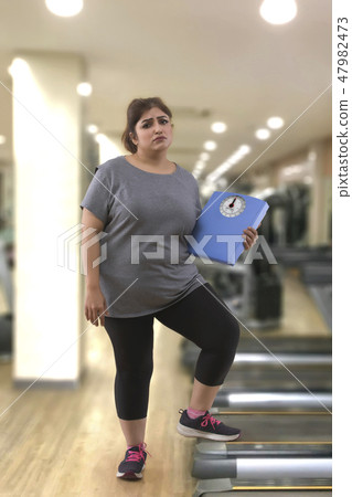 fat woman in a gym holding a weight scale 47982473