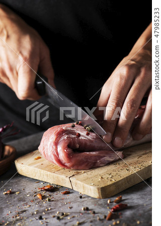 man cutting a piece of pork tenderloin 47985233