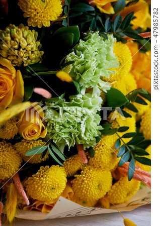 Yellow bouquet with green carnation, in the composition of chrysanthemums, roses and dyed grains 47985782