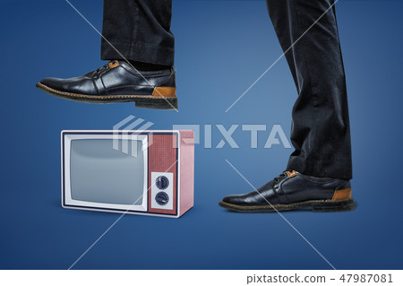 A giant businessman's leg stepping on a small retro TV box with an empty screen. A giant businessman's leg stepping on a small retro TV box with an empty screen. 47987081