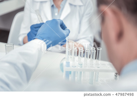 Scientist putting liquids tnto test tubes with pipette Scientist putting liquids tnto test tubes with pipette 47987498