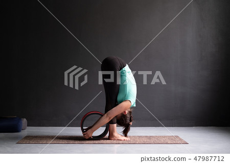 woman practicing yoga, doing forward bend exercise using wheel, uttanasana pose 47987712