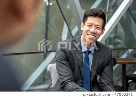 Smiling Asian businessman sitting at office lounge Smiling Asian businessman sitting at office lounge 47990271