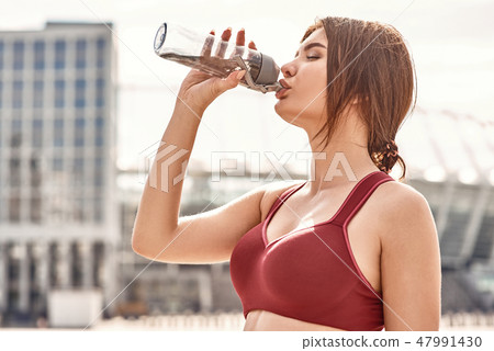 Fresh water after good workout. Side view of young beautiful woman drinking fresh water after active Fresh water after good workout. Side view of young beautiful woman drinking fresh water after active 47991430