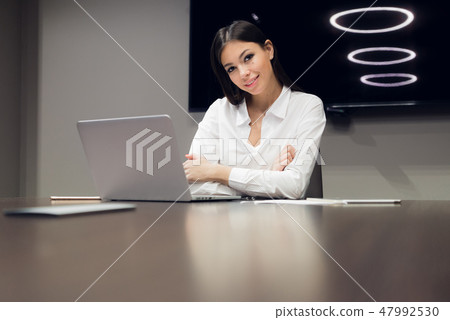 Portrait of a cheerful businesswoman sitting at the table in office and looking at camera Portrait of a cheerful businesswoman sitting at the table in office and looking at camera 47992530