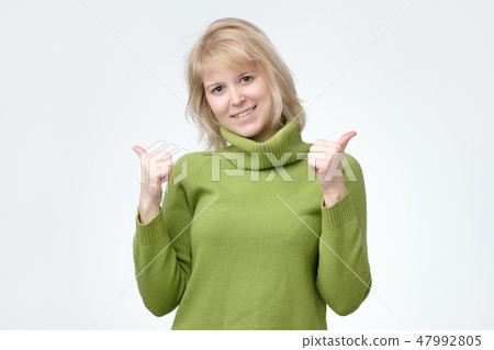 Happy young caucasian female wearing green sweater making thumb up sign and smiling cheerfully Happy young caucasian female wearing green sweater making thumb up sign and smiling cheerfully 47992805