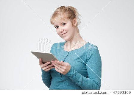 Pretty charming blonde woman in blue shirt having tablet in hands looking at camera 47993309