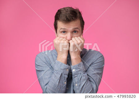 Man looks scared in the camera and presses his fists to his mouth in a sign of fear and fright. Man looks scared in the camera and presses his fists to his mouth in a sign of fear and fright. 47993820