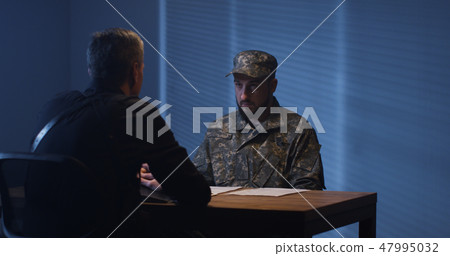 Expressive policeman examining military man in interview room Expressive policeman examining military man in interview room 47995032