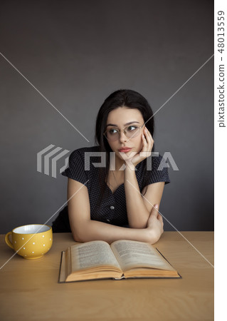 Beautiful young woman in glasses reading a book. 48013559