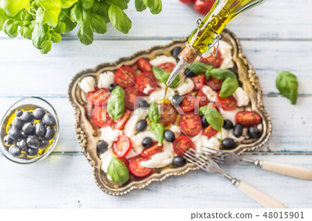 Pouring olive oil on caprese salad.  48015901