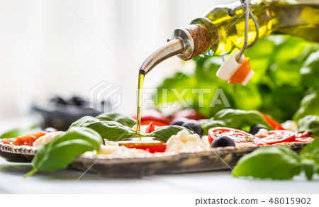 Pouring olive oil on caprese salad.  48015902