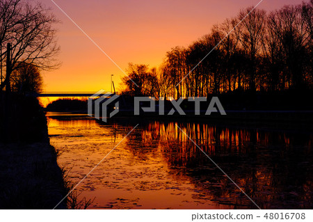 Dramatic and colorful sunrise over a Beautiful early winter landscape with a frozen river Dramatic and colorful sunrise over a Beautiful early winter landscape with a frozen river 48016708