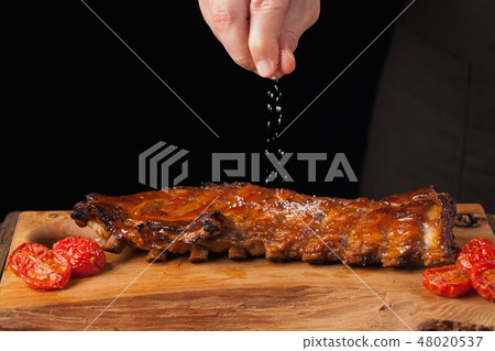 The chef sprinkles salt in ready to eat pork ribs. 48020537
