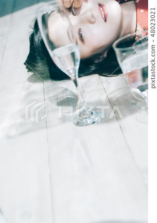 A glass of water and a red one piece lying down on the floor 48023021