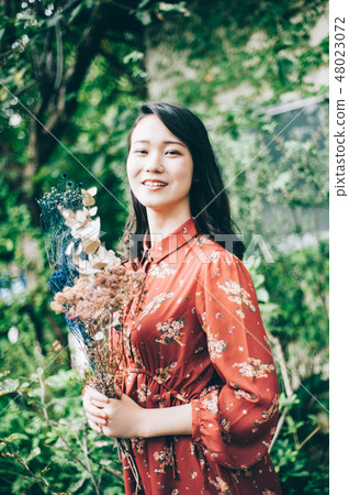 A red one-piece lady with a bouquet in the garden A red one-piece lady with a bouquet in the garden 48023072
