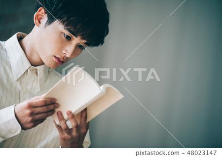 A man with a white shirt reading a book by the window A man with a white shirt reading a book by the window 48023147