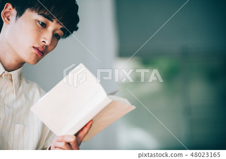 A man with a white shirt reading a book by the window A man with a white shirt reading a book by the window 48023165