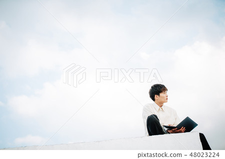 A man sitting on the roof and opening a laptop 48023224