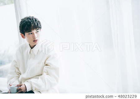 A man leaning at the window by the hand with a mug 48023229