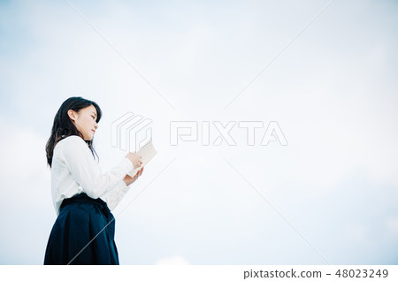 A woman in white shirt reading a book standing on the roof A woman in white shirt reading a book standing on the roof 48023249